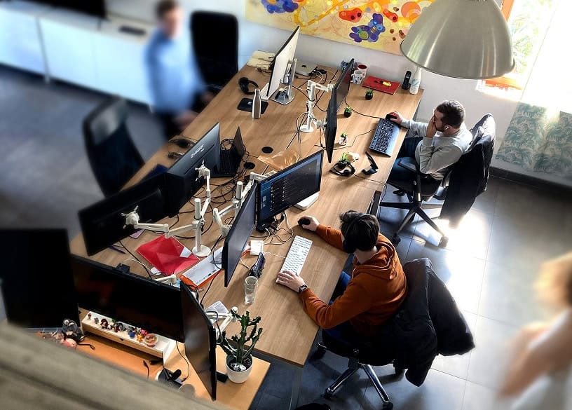 Travail en bureau avec plusieurs employés utilisant des ordinateurs, ambiance moderne et collaboration, espace de travail technologique, environnement professionnel dynamique.